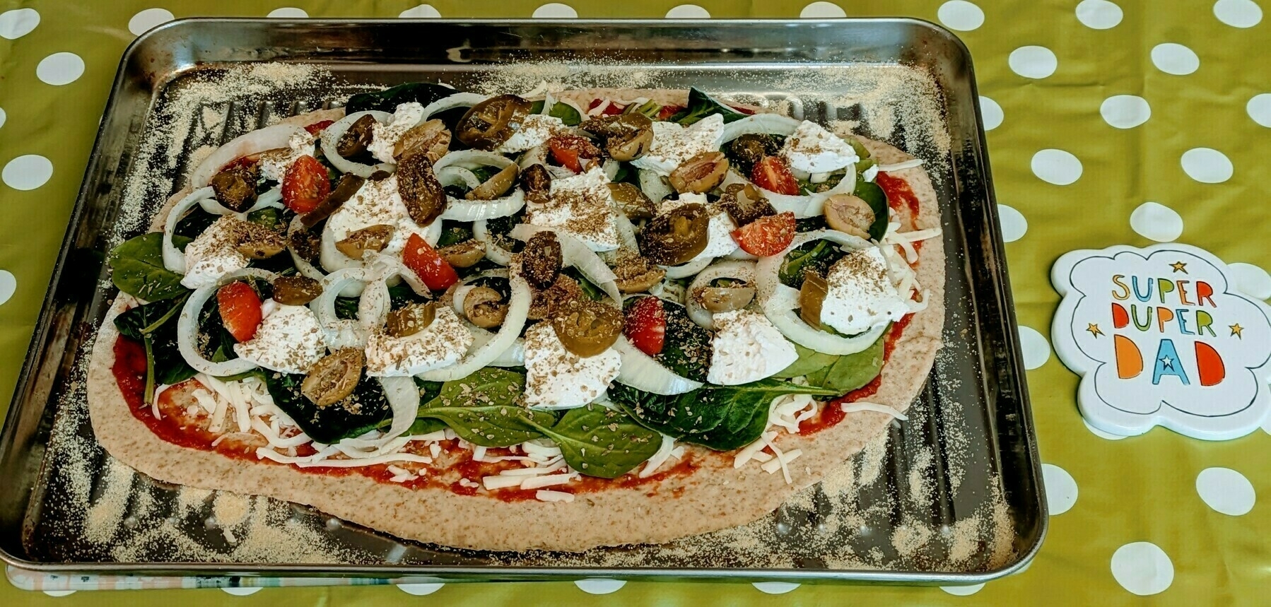 A homemade pizza topped with vegetables and cheese is placed on a baking tray with a "Super Duper Dad" card beside it.